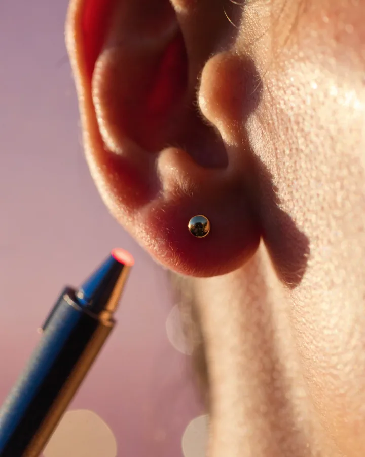 Lóbulo com joia de ouro e caneta de laser próxima